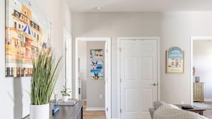 A bedroom with a bed, a dresser, a potted plant, and a door leading to another room.