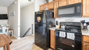 A modern kitchen with a black refrigerator, wooden cabinets, a microwave, and a stove.