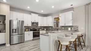 A modern kitchen with white cabinets, stainless steel appliances, a granite countertop, and bar stools. - Royal Retreat: All Inclusive Champions Gate Resort 6BD6BA Free Heated Pool Villa (Four Corners)