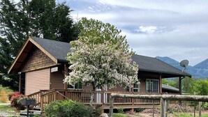 Een houten chalet met terras, omringd door weelderige begroeiing en een berg op de achtergrond.