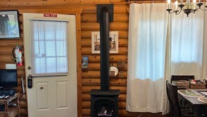 A log cabin interior with a fireplace, a fire exit sign, a dining area, and a television.