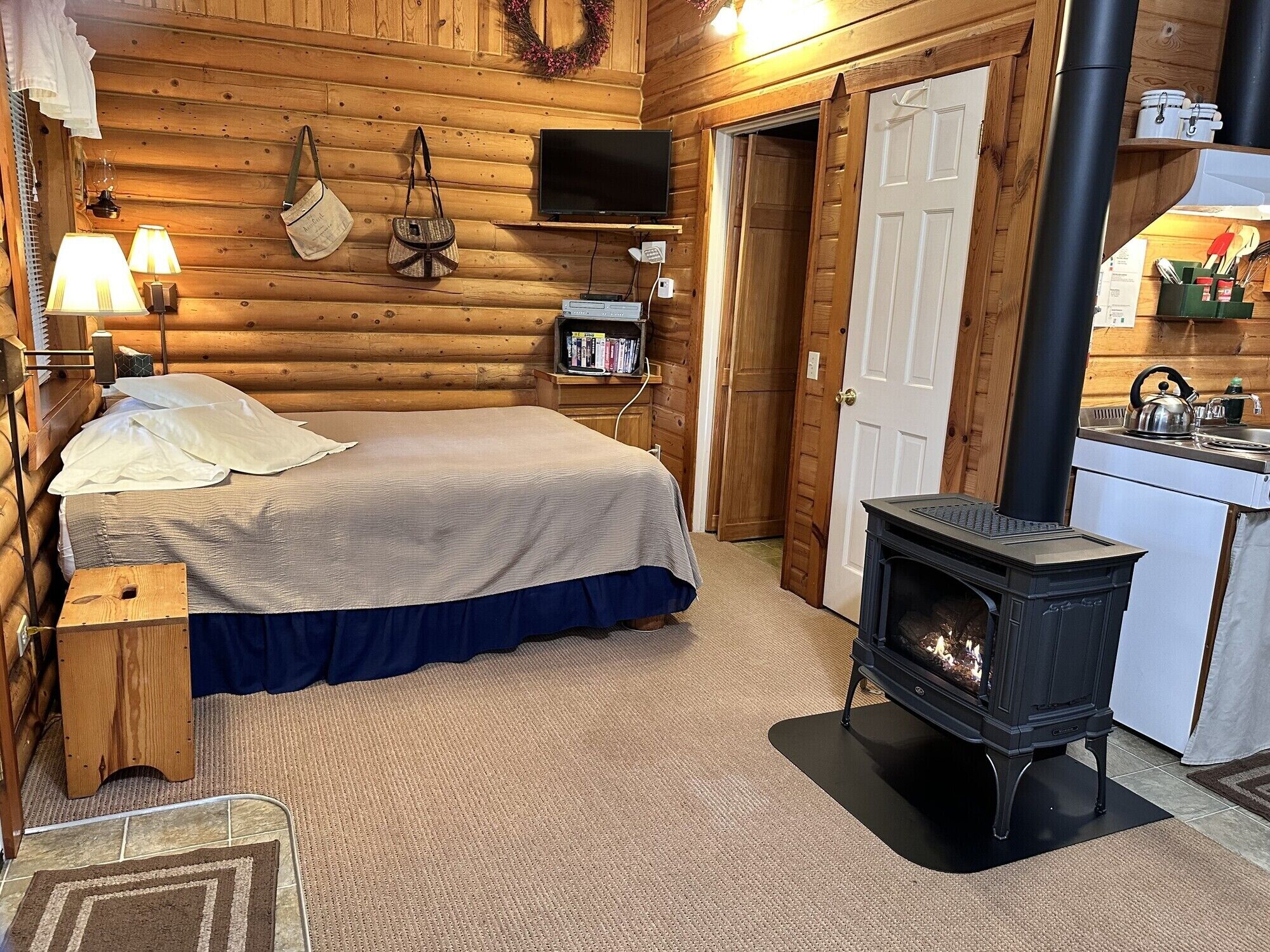 Une chambre aménagée dans un chalet en rondins, comprenant un lit, une cheminée, une télévision et un petit coin cuisine.