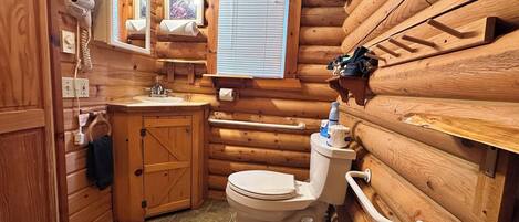 A log cabin bathroom with a wooden sink, toilet, and a mirror.