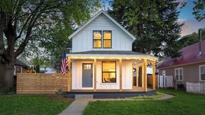 A two-story house with a covered porch, a flag, and a well-maintained lawn. - Dwntwn CDA Historic Remodel - Walk to Lake with Hot Tub! (Coeur d'Alene)