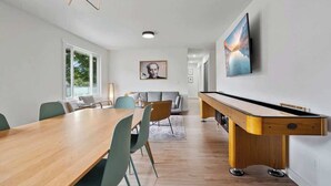 Ein modernes Wohnzimmer mit einem Holzesstisch, grünen Stühlen, einem Billardtisch und einem großen Gemälde an der Wand.