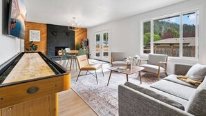 Ein modernes Wohnzimmer mit Billardtisch, bequemen Sitzgelegenheiten, Kamin und großen Fenstern mit Blick ins Freie.