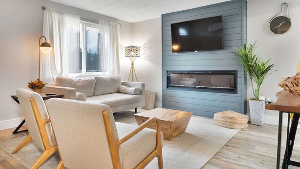 Un soggiorno moderno con un divano grigio, un tavolino in legno e una televisione a schermo piatto montata su una parete blu.