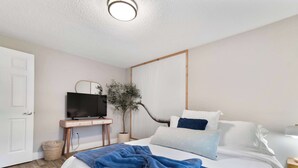 Una camera da letto ordinata con un letto, una televisione su un mobile in legno, una pianta in vaso e una porta bianca.