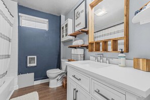 Un baño moderno con pared azul de acento, sanitarios blancos, un espejo grande y cortina de ducha.