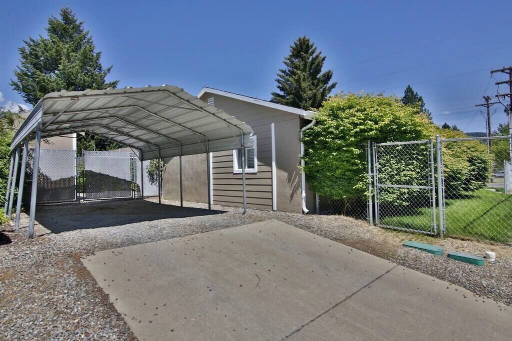 Un garage fermé avec une allée en gravier, une clôture en métal et une maison en arrière-plan.