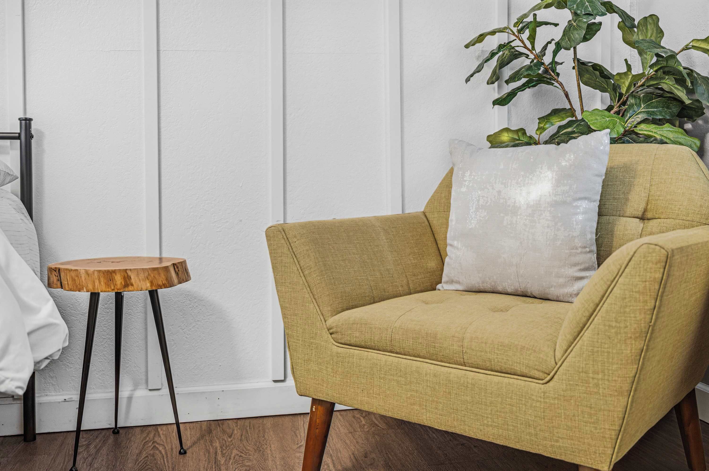 A room with a yellow armchair, a small wooden side table, and a potted plant.