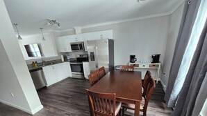 A modern kitchen with white cabinets, stainless steel appliances, and a dining area with a wooden table and chairs.