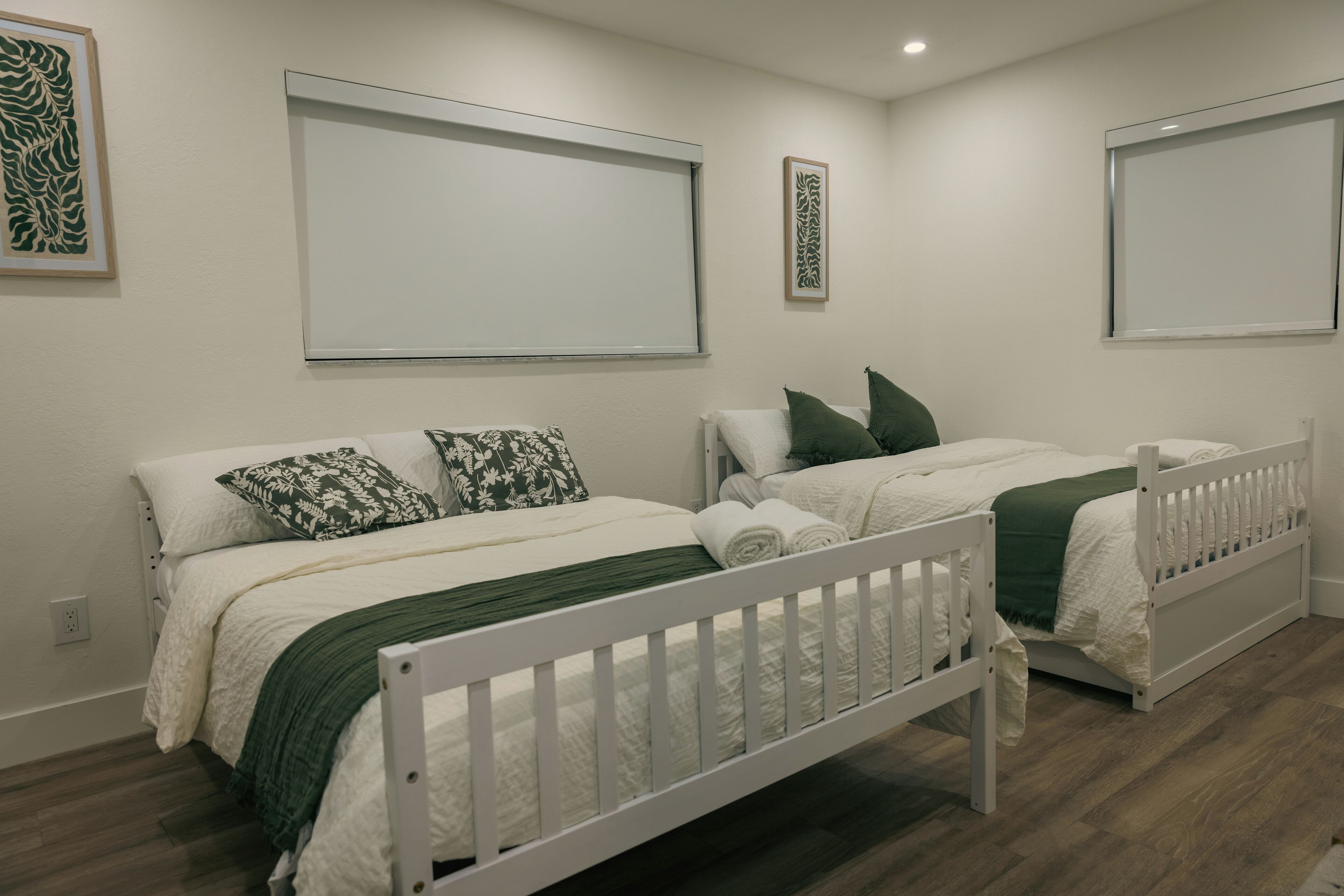 Ein Schlafzimmer mit zwei Betten, weißer Bettwäsche, grünen Kissen und einem weißen Babybett.
