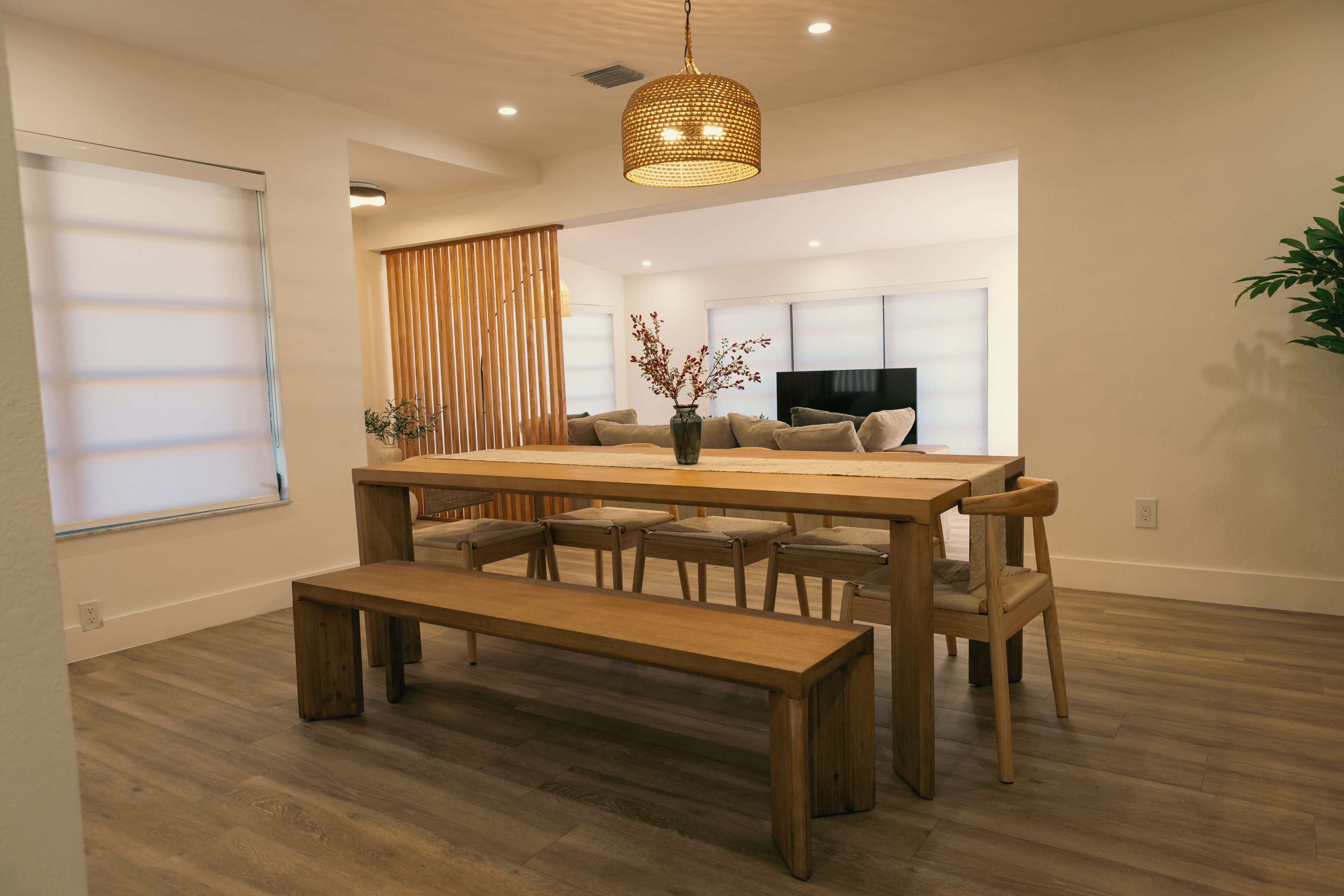 A modern dining area with a wooden table, benches, and a hanging light fixture.