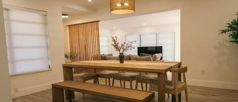 A modern dining area with a wooden table, benches, and a hanging light fixture.