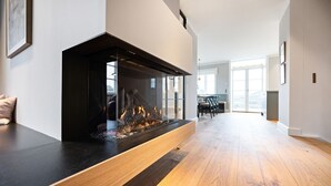 Una sala de estar moderna con chimenea de vidrio, piso de madera y un comedor al fondo.