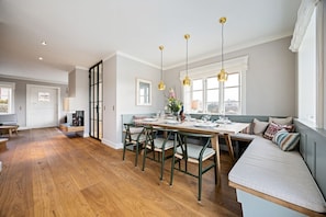 Una cocina amplia con suelo de madera, un comedor con una mesa larga y sillas, y una zona de estar con un banco y cojines.