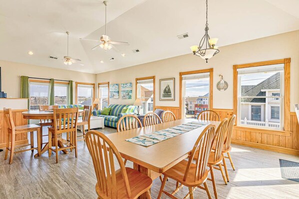 A spacious dining area with a wooden table and chairs, a sofa, and a view of the city through large windows.