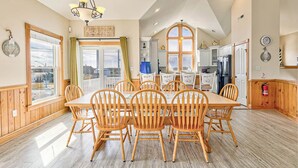 A spacious dining area with a wooden table and chairs, a chandelier, and large windows offering views.