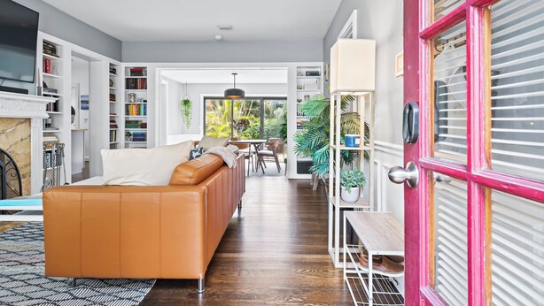 A modern living room with a leather sofa, open shelving with books, a dining area, and a view of greenery outside. - Charming 3-bedroom house with WiFi, AC in welcoming Lake Worth Beach (Lake Worth Beach)
