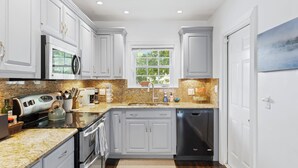 A modern kitchen with white cabinets, stainless steel appliances, a granite countertop, and a window with a view of greenery. - Charming 3-bedroom house with WiFi, AC in welcoming Lake Worth Beach (Lake Worth Beach)