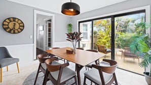 A modern dining area with a wooden table and chairs, a large wall clock, and a view of a garden through a sliding glass door. - Charming 3-bedroom house with WiFi, AC in welcoming Lake Worth Beach (Lake Worth Beach)