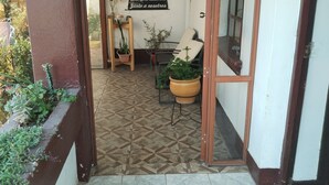 Un passadís amb sòl de rajola que condueix a una habitació amb un cartell, una cadira i una planta en test.