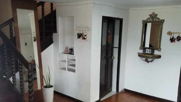Una habitació àmplia amb sòl de fusta, unes escales, una paret blanca amb un mirall i una porta.