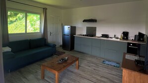 Ein modernes Wohnzimmer mit einer Couch, einem Holztisch und einer Küchenzeile mit Schränken und Geräten.
