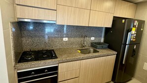 Une cuisine moderne dotée de plans de travail en granit, d’appareils électroménagers en acier inoxydable et de meubles de rangement en bois clair.
