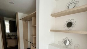 Un couloir avec un plancher en bois, un placard doté de plusieurs étagères et un miroir accroché au mur.