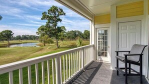 Ein Balkon mit Blick auf einen Golfplatz, eine Tür und ein Stuhl.