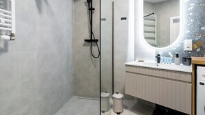 Casa de banho moderna com cabine de duche, espelho grande e toucador com produtos de higiene pessoal.