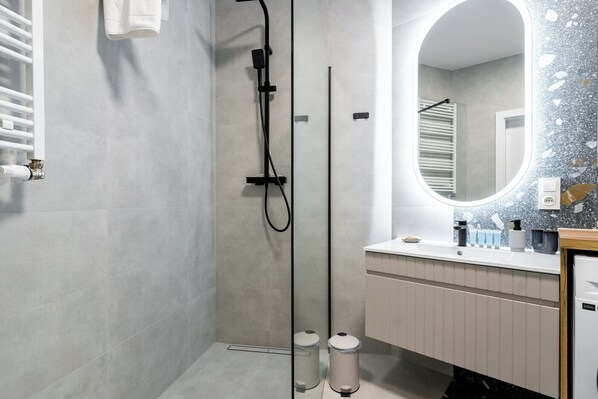 Een moderne badkamer met een inloopdouche, een grote spiegel en een wastafel met toiletartikelen.