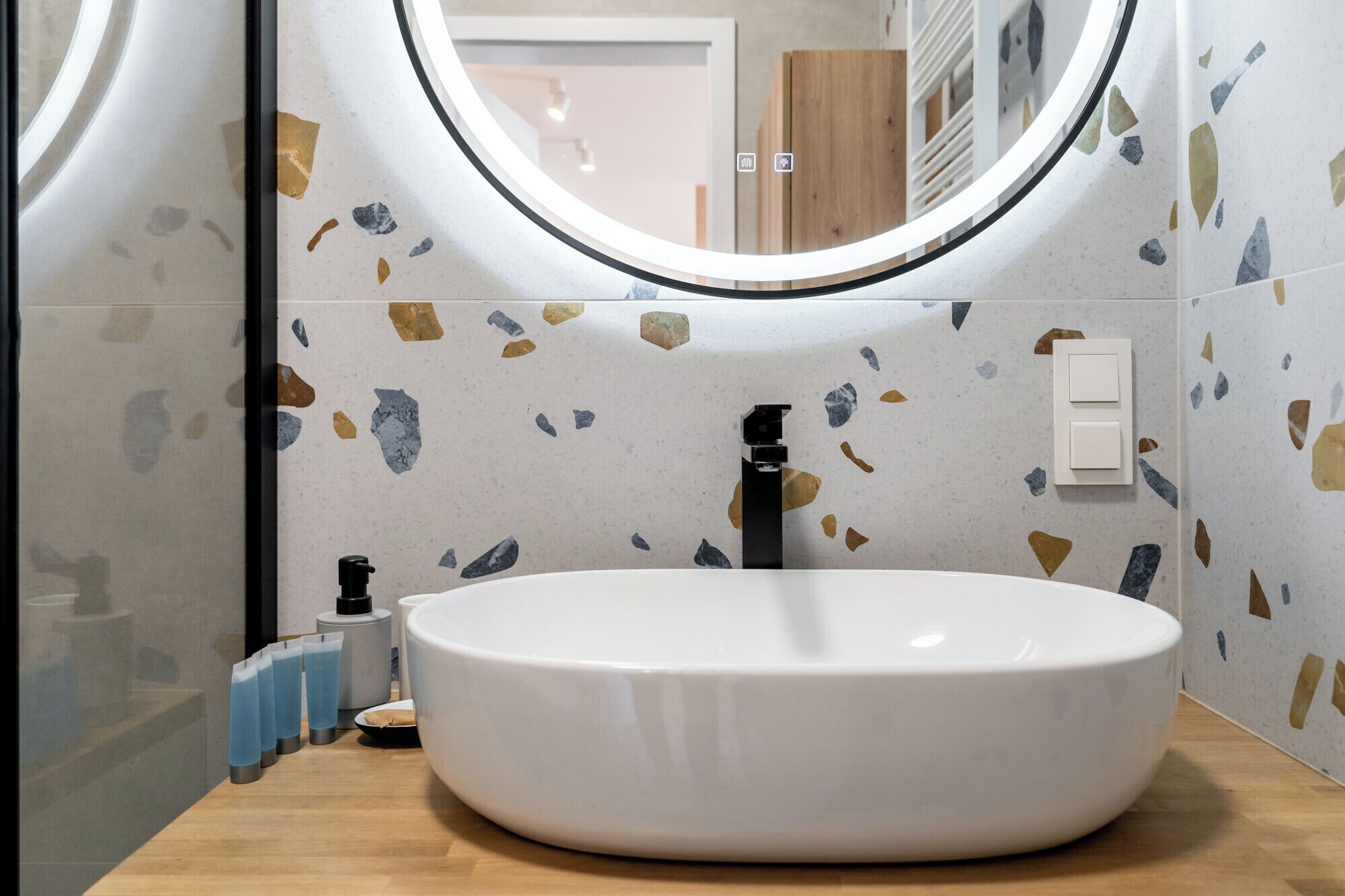 Un bagno con uno specchio rotondo, un lavandino bianco e una parete con decorazione a terrazzo.