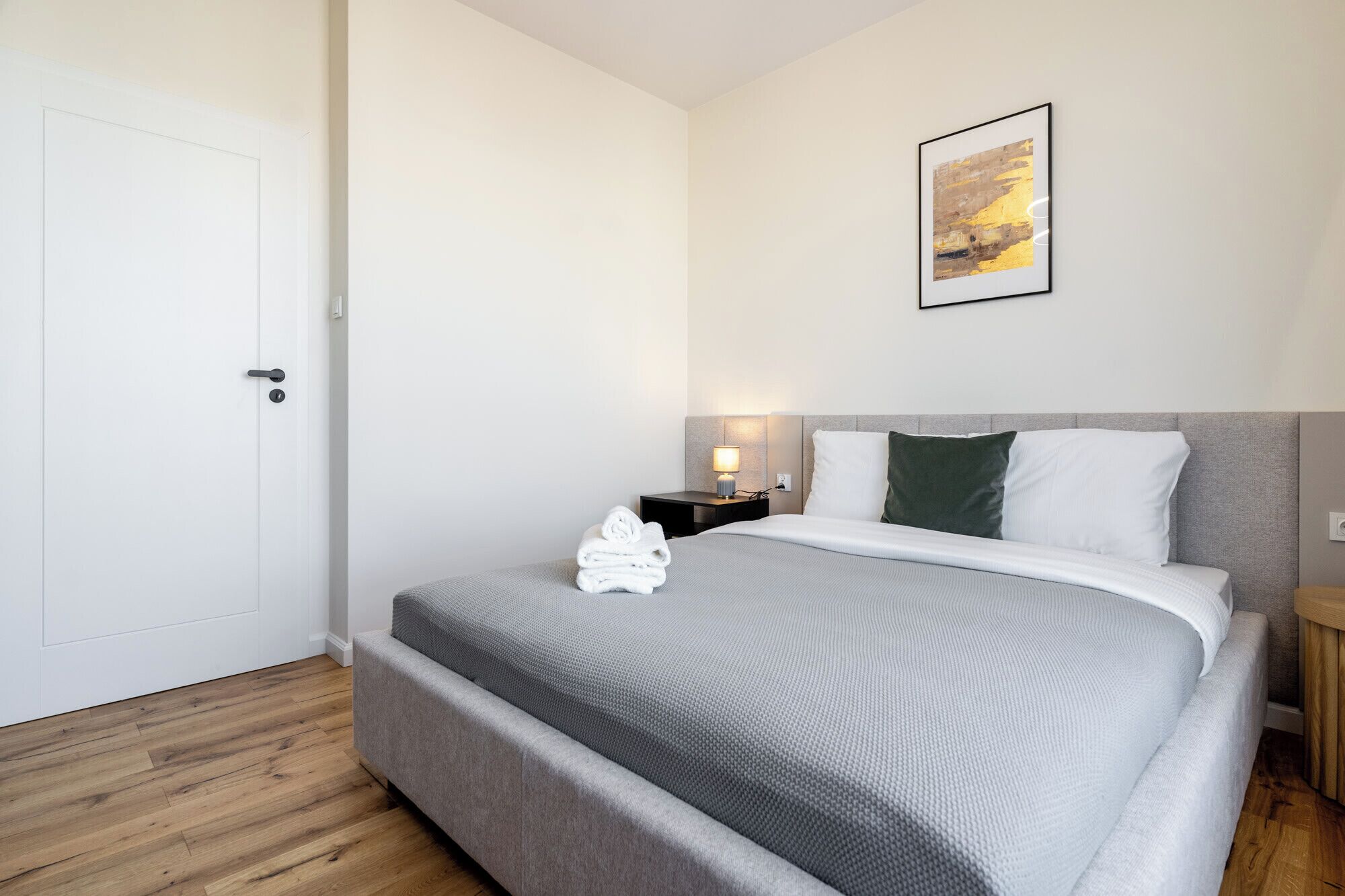 Una habitación de hotel con una cama, una mesita de noche, una lámpara de pared y un cuadro enmarcado.