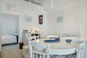 Una habitación con cama, una mesa de comedor con sillas, un reloj y obras de arte en las paredes.