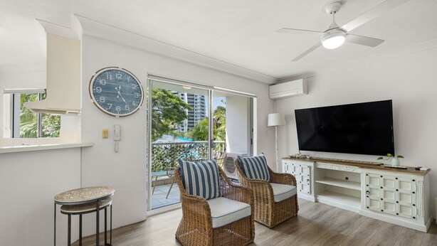 A living room with wicker furniture, a flat-screen TV, and a large clock on the wall. - Cosy Central Burleigh Getaway (Burleigh Heads)