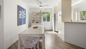 A modern kitchen with white cabinetry, a dining table, and a ceiling fan. - Cosy Central Burleigh Getaway (Burleigh Heads)