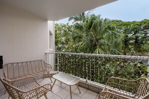 A balcony with wicker chairs and a small table, surrounded by a white railing and lush greenery. - Cosy Central Burleigh Getaway (Burleigh Heads)