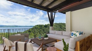 Un balcon aménagé avec un canapé, des chaises et une petite table, offrant une vue panoramique sur un lac et une forêt.