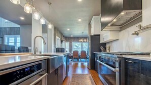 Une cuisine moderne dotée d’appareils électroménagers en acier inoxydable, d’un îlot central et de luminaires suspendus.
