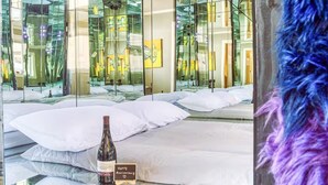 Habitación de hotel con un espejo grande que refleja el interior, una botella de vino y un pequeño cartel sobre la cama.