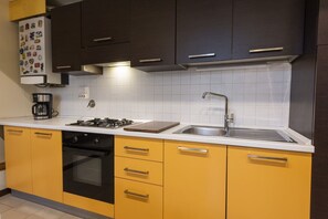 Een koelkast, een oven, een kookplaat, kookgerei, borden en bestek