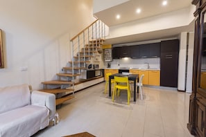 Een moderne keuken met donkere kastjes, een eethoek met gele stoelen, en een trap naar een hoger niveau.