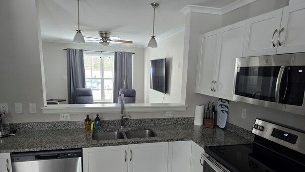 A modern kitchen with white cabinets, stainless steel appliances, a granite countertop, and a window with curtains. - Acadia Villas!  3A Olivia.  A private neighborhood nestled in the woods. (Trenton)