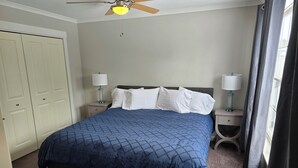 A bedroom with a bed, two bedside tables, a ceiling fan, and a window with curtains. - Acadia Villas!  3A Olivia.  A private neighborhood nestled in the woods. (Trenton)