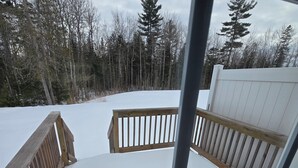 A wooden deck with a railing, surrounded by snow and trees. - Acadia Villas!  3A Olivia.  A private neighborhood nestled in the woods. (Trenton)