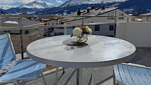 Een ronde tafel met een bloevas op een balkon met uitzicht op besneeuwde bergen.