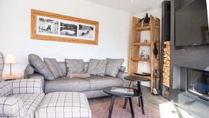 Een moderne woonkamer met een grijze bank, een bijpassende fauteuil, een klein rond tafeltje en een open haard.